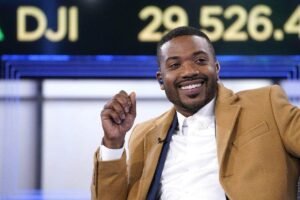 Ray J smiling during a live TV appearance wearing a brown coat