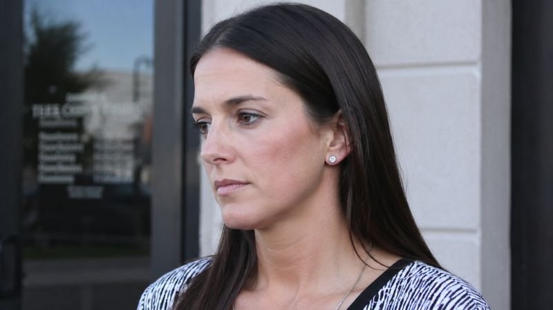 Serious-looking woman standing outside a building entrance, symbolizing Jessica Dorrell’s resignation and the fallout from the Arkansas football scandal.