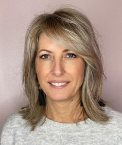 Woman over 60 with fine hair styled in a shoulder-length layered haircut with side-swept bangs adding volume and fullness